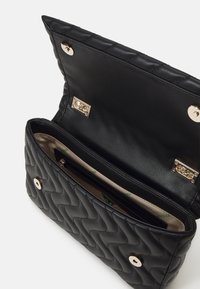 Bolso de mano de cuero acolchado negro con una textura suave, detalles metálicos en dorado y un único compartimento con cremallera. Se abre con un cierre a presión.
