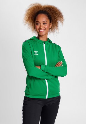 Grøn zip-up hoodie med en hvid lynlås, sorte accenter på skuldrene og et logo på brystet. Stoffet har en tekstureret overflade.