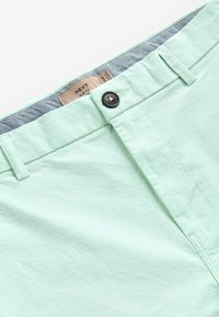 Șorturi slim-fit de culoare verde mentă deschisă, cu un finisaj texturat, închidere cu nasture și un brâu interior cu model pentru un detaliu suplimentar. Etiqueta mărcii este vizibilă.