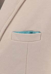 Beige Sakko mit Revers und einer Brusttasche, die ein ordentlich gefaltetes hellblaues Taschentuch enthält.