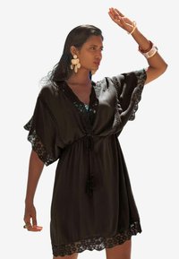 Kaftan noir avec bordure en dentelle, manches courtes volantées, décolleté en V et taille à cordon. Tissu léger avec une silhouette fluide.