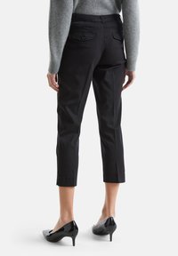 Czarne krótkie spodnie o gładkiej fakturze, z tylnymi kieszeniami i dopasowanym krojem, połączone z błyszczącymi czarnymi szpilkami.