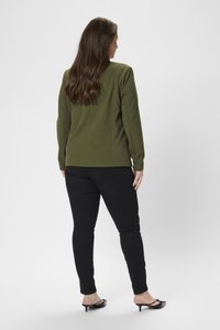 Blazer vert olive avec des épaules structurées, associé à un jean noir skinny et des talons noirs. Design simple avec une texture de tissu lisse.