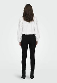 Blusa blanca con detalles de calados en las mangas, combinada con jeans ajustados negros y botines negros de tacón. Diseño simple y limpio.