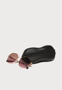 Ochelari de soare cu lentile hexagonale roz și rame din metal aurit, așezați pe un toc negru cu fermoar inscripționat "vogue."