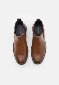 Chaussures en cuir marron à enfiler avec une finition lisse, un bout arrondi et des détails de couture minimaux. Panneaux latéraux élastiques pour un enfilage facile.