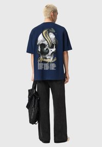 Granatowy, oversize'owy t-shirt z dużą grafiką czaszki, węża, kwiatowymi akcentami i napisem. W połączeniu z czarnymi, szerokimi spodniami i torebką.