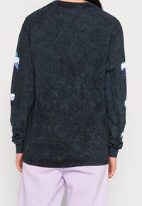 Černá košile s dlouhým rukávem ze vyblednuté, texturované tkaniny. Obsahuje barevné grafické vzory na obou rukávech. Klasický kulatý výstřih.