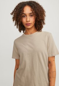Beige katoenen t-shirt met korte mouwen en een ronde hals. Zachte textuur en een ontspannen pasvorm, met subtiele stikdetails.