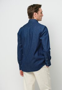 Camicia di denim blu scuro con colletto classico, maniche lunghe e polsini con bottone. Presenta uno sprone posteriore con piega per un maggiore movimento.