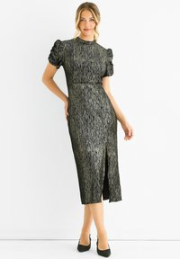 Black and gold-patterned midi dress with short puffed sleeves, high neckline, fitted waist, and a side slit; smooth, textured fabric.