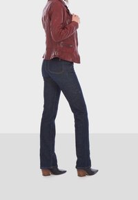 Rote Lederjacke mit strukturiertem Finish, kombiniert mit dunkelblauen skinny Jeans und schwarzen Knöchelstiefeln mit blockiertem Absatz.