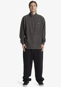 Dark gray, quarter-zip pullover sweatshirt with textured fabric, kangaroo pocket, and small logo. Paired with loose black pants and sneakers.