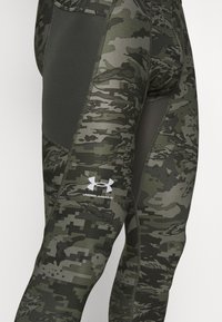 Zielone legginsy w kamuflażu z mieszanką ciemnoszarych tonów. Posiadają gładką fakturę, dopasowany krój oraz białe logo Under Armour.
