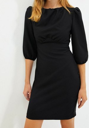 Zwarte kokerjurk met pofmouwen en een plooibuste. Soepele stof, tot de knie, eenvoudig ontwerp zonder zichtbare patronen of accenten.