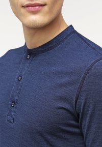 Námořnická modrá košile typu henley vyrobená z měkké látky, s kulatým výstřihem, plaketou se třemi knoflíky a jemnou texturou.