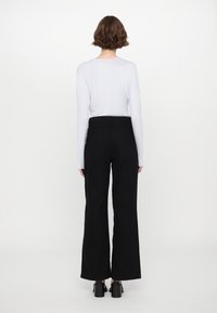 Maglietta azzurra a maniche lunghe abbinata a pantaloni neri a vita alta con gamba larga e scarpe con tacco nere, vista da dietro.