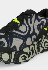 Baskets noires et grises avec des motifs ondulés abstraits, logo jaune néon et maintien de lacets, et semelle à motifs assortie au design supérieur.