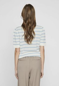 Suéter de punto con mangas cortas, que presenta rayas azules y blancas y una tela texturizada. Combinado con pantalones de corte relajado en marrón claro.