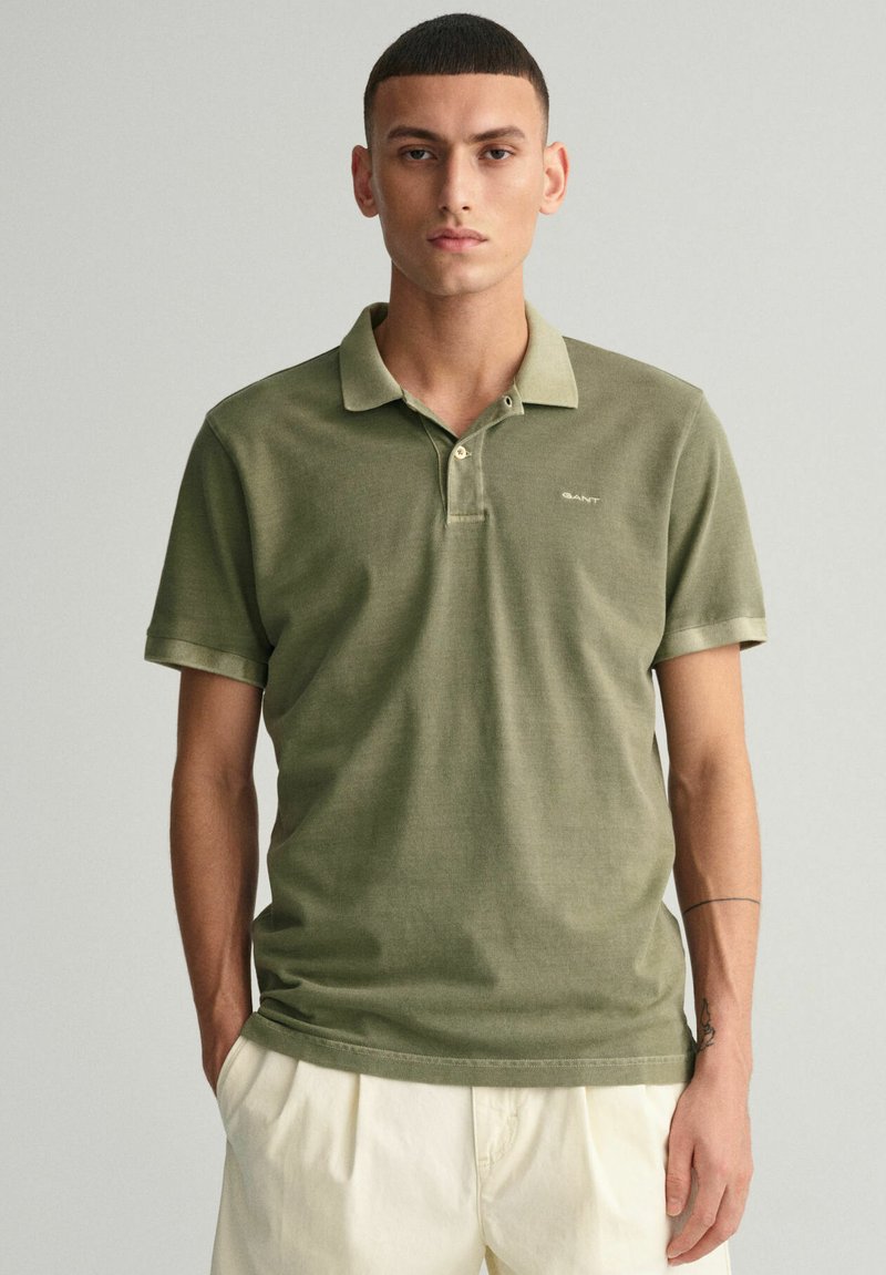 Polo-shirt vert olive à manches courtes, avec un plastron à deux boutons et un logo discret. Tissu en coton lisse avec un col classique.