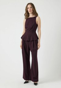 Burgundy peplumtop med vertikala ränder, parat med matchande vida byxor. Slät textur, ärmlös design och spetsiga stiletthälar.