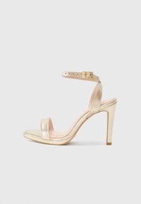 Goldfarbene, metallische High-Heel-Sandalen mit einem einzelnen Zehenriemen und einem Knöchelriemen, der mit einer quadratischen Schnalle versehen ist. Glatte Textur und elegantes Design.