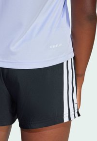 Camiseta deportiva AEROREADY de color púrpura claro con tejido texturizado, combinada con pantalones cortos negros que presentan franjas verticales blancas.