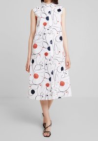 Abito bianco senza maniche con bottoni frontali, caratterizzato da una stampa astratta con cerchi e linee in navy, rosso e nero; design di lunghezza media.