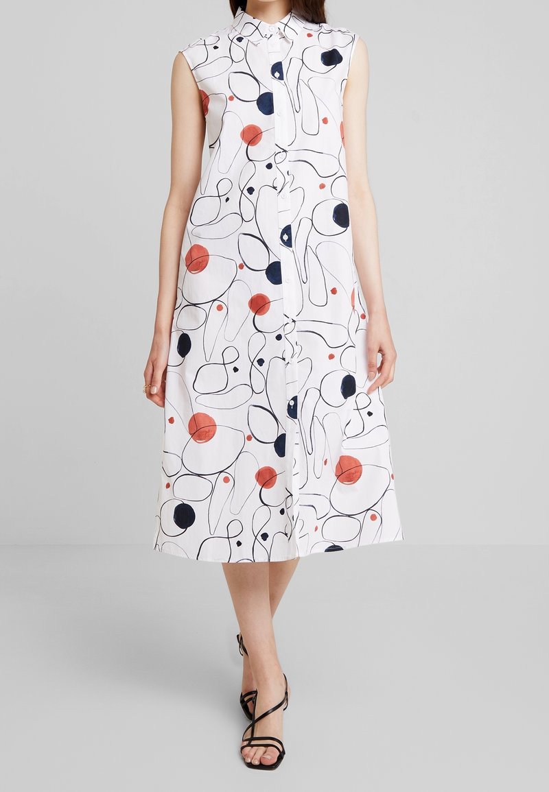Abito bianco senza maniche con bottoni frontali, caratterizzato da una stampa astratta con cerchi e linee in navy, rosso e nero; design di lunghezza media.