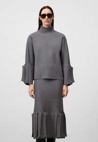 Maglione grigio a maglia con colletto alto e maniche a campana, abbinato a una gonna midi coordinata con bordo plissettato.