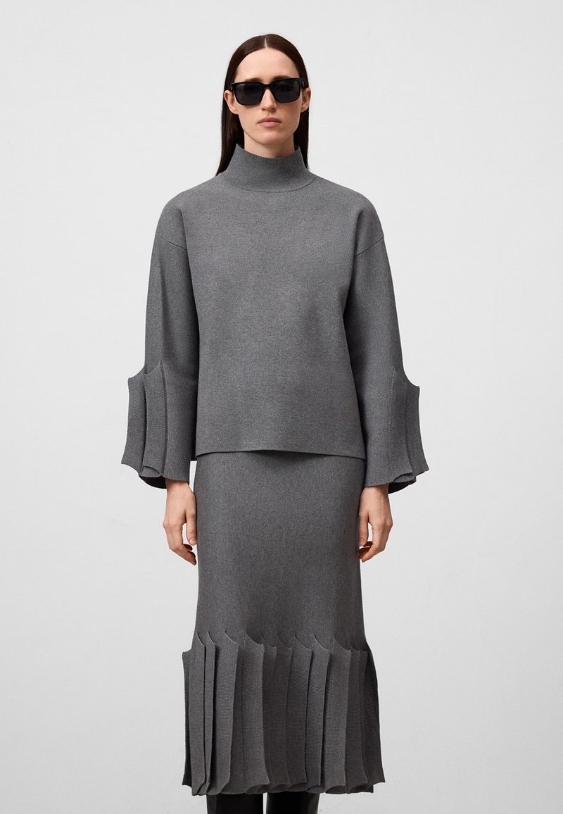 Maglione grigio a maglia con colletto alto e maniche a campana, abbinato a una gonna midi coordinata con bordo plissettato.