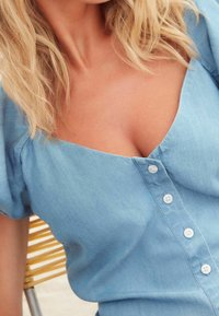 Helle blaue Denim-Bluse mit V-Ausschnitt, kurzen Puffärmeln und Knöpfen vorne. Weicher Stoff mit lässigem Design.