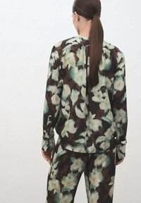 Blusa con estampado floral y pantalones a juego en tonos marrón oscuro, verde y blanco; tejido transparente con un corte relajado y detalles de botones en las mangas.