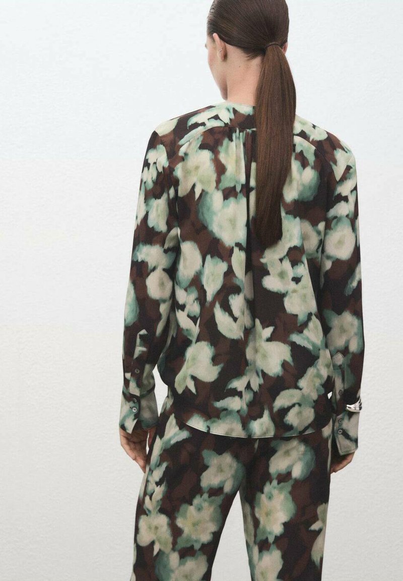 Blusa con estampado floral y pantalones a juego en tonos marrón oscuro, verde y blanco; tejido transparente con un corte relajado y detalles de botones en las mangas.