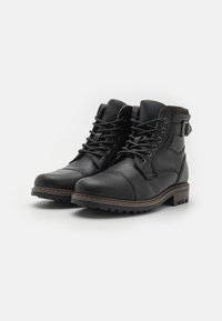 Botas de cuero negro hasta el tobillo con cordones en la parte delantera, detalles de costura, puntera redonda y suela de goma. Presentan un hebilla lateral y acentos marrones.