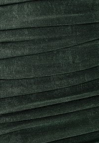 Tumma vihreä kankaan ribbitekstuuri vaakasuorilla poimuilla, joka esittelee raskaasti tekstuuripintaa ja pehmeää kiiltoa. Kankaan pinta vaikuttaa tasaiselta ja yhtenäiseltä.