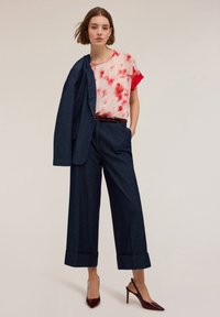 Kulot denim lebar, warna gelap, dipadukan dengan blouse tie-dye merah dan pink. Dipakai dengan sepatu hak tinggi burgundy dan blazer navy yang dirancang dengan baik.