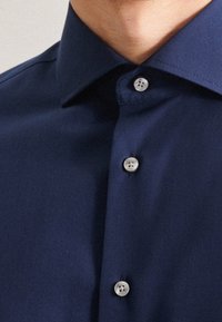 Marinblå knappar-mitt skjorta med spetsig krage, flerknappad placket och slät tygtextur med subtil glans.