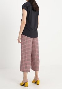 Černý top s krátkými rukávy, červeno-bílé kostičkované široké kalhoty a žluté lodičky na blokovém podpatku, pohled zezadu.