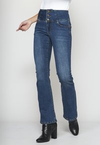 Högmidjade blå denimjeans med femknappsstängning, lätt blekning och prydliga fickor. Har en utsvängd ben-design.
