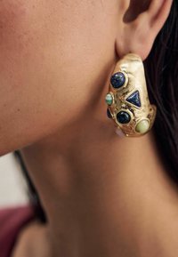 Ohrringe in goldfarbener Ausführung mit verschiedenen Edelsteinen, darunter blaue und grüne Steine, in einem strukturierten, abstrakten Design mit dreieckigen Formen.