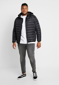 Black puffer jacket with a zip closure, hood, and ribbed cuffs. Worn over a white t-shirt with gray slim-fit jeans and black sneakers.