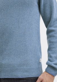 Light blue sweater made of soft fabric. Features ribbed cuffs and hem, with a small branded tag on the side. Simple, classic design.