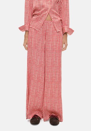 Czerwono-białe luźne spodnie w kratę oraz dopasowany top z podwiniętymi mankietami, noszone z ciemnobrązowymi sznurowanymi butami.