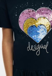 Crna majica s kratkim rukavima s motivom srca od višebojnih šljokica (roza, žuta, plava) i izvezenim tekstom "desigual" u srebrnoj boji ispod grafike.
