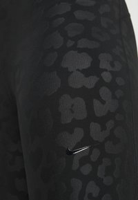 Czarne legginsy z delikatnym wzorem w panterkę, wykonane z elastycznego materiału. Zawierają małe srebrne logo Nike po boku.