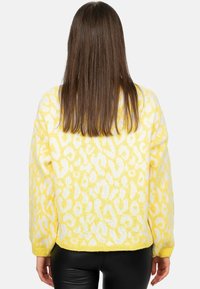 Geel gebreide trui met witte luipaardprint, losse pasvorm en geribde manchetten. De textuur lijkt zacht en pluizig. De zoomlijn is recht en reikt tot de taille.