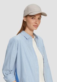 Hellgraue Baseballmütze mit besticktem Text, kombiniert mit einem blau-weiß gestreiften Hemd mit Knöpfen. Weicher Stoff und lässige Passform.