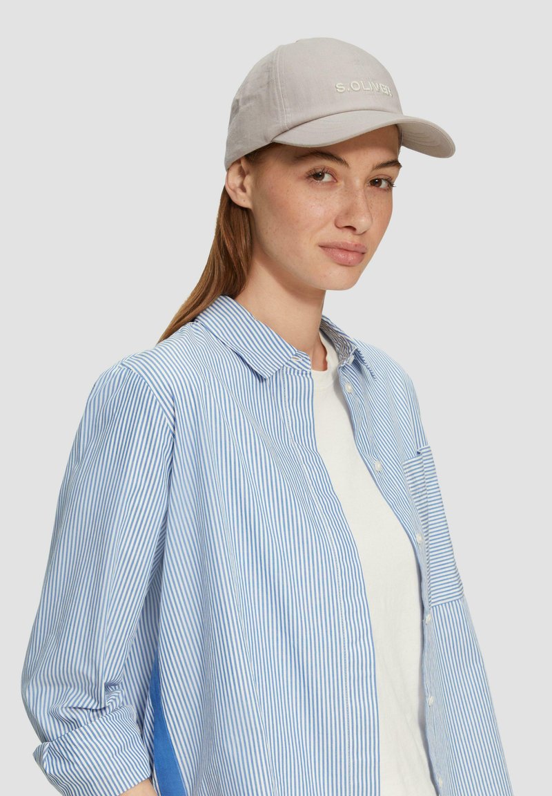 Hellgraue Baseballmütze mit besticktem Text, kombiniert mit einem blau-weiß gestreiften Hemd mit Knöpfen. Weicher Stoff und lässige Passform.