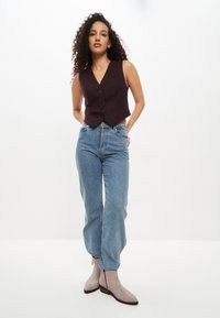 Vest cu dungi bordeaux, scurt, cu nasturi, asociat cu blugi largi de un albastru deschis și cizme scurte din suede gri. Elemente de design simple.